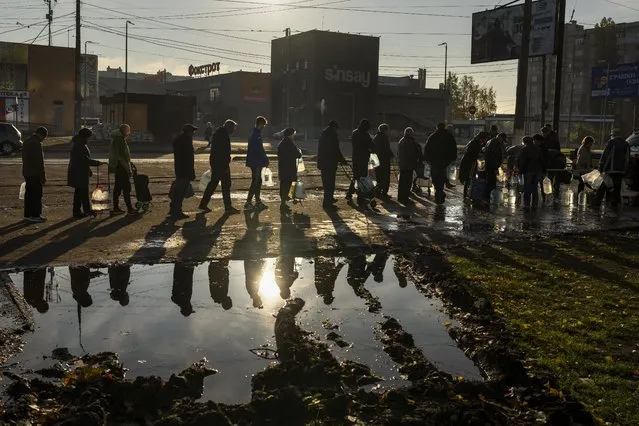 People queuing up hold plastic bottles to refill drinking water from a tank in the center of Mykolaiv, Monday, October 24, 2022. Since mid-April, citizens of Mykolaiv, with a pre-war population of half a million people, have lived without a centralized drinking water supply. Russian Forces cut off the pipeline through which the city received drinking water for the last 40 years. (Photo by Emilio Morenatti/AP Photo)
