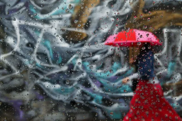 A woman walks past graffiti on a wall in the Williamsburg neighborhood of the borough of Brooklyn, in New York, September 16, 2014. The picture was taken through car window with raindrops. (Photo by Shannon Stapleton/Reuters)