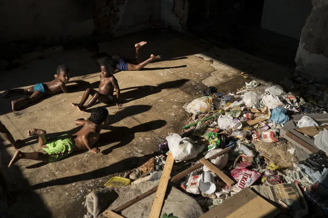 In this September 10, 2017 photo, children slide on a puddle near trash as they play in a squatter building that used to house the Brazilian Institute of Geography and Statistics (IBGE) in the Mangueira slum of Rio de Janeiro, Brazil. Toddlers roam in the abandoned building where mounds of trash create pockets of stench. (Photo by Felipe Dana/AP Photo)