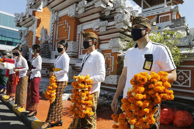 Airport officers wearing face masks line up as they hold flowers to welcome passengers at Bali airport, Indonesia on Friday, July 31, 2020. (Photo by Firdia Lisnawati/AP Photo)