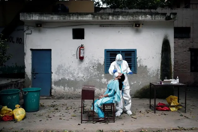 A health worker in personal protective equipment (PPE) collects a sample using a swab from a person at a school which was turned into a centre to conduct tests for the coronavirus disease (COVID-19), amidst the spread of the disease, in New Delhi, India, August 6, 2020. (Photo by Adnan Abidi/Reuters)