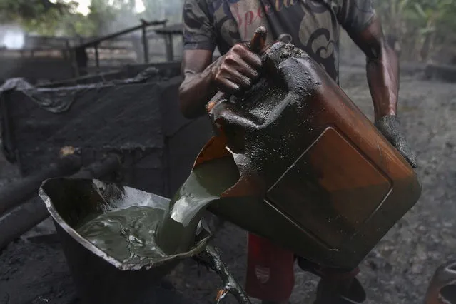 A worker pours crude oil into a locally made burner using a funnel at an illegal oil refinery site near river Nun in Nigeria's oil state of Bayelsa November 25, 2012. Thousands of people in Nigeria engage in a practice known locally as “oil bunkering” – hacking into pipelines to steal crude then refining it or selling it abroad. The practice, which leaves oil spewing from pipelines for miles around, managed to lift around a fifth of Nigeria's two million barrel a day production last year according to the finance ministry. (Photo by Akintunde Akinleye/Reuters)
