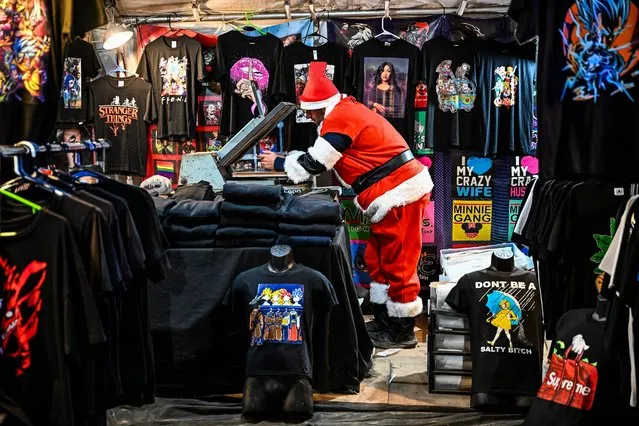 A man dressed as Santa Claus waits for customers at his t-shirt shop at Santa's Enchanted Forest in Miami, Florida, on December 24, 2022. (Photo by Chandan Khanna/AFP Photo)