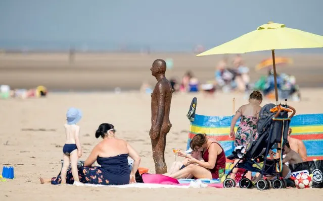 People and a statue are seen on Crosby Beach as the spread of the coronavirus disease (COVID-19) continues, Crosby, Britain on August 13, 2020. (Photo by Peter Powell/The Telegraph)