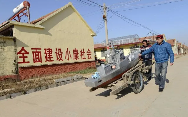 Residents push a cart to transport a homemade replica of a destroyer vessel made by retired fishboat captain Guo Changhai (not pictured), as they walk along a road after a test run in Xiaojia village of Rizhao, Shandong province, December 13, 2014. Guo, 56-year-old, who sold his fishboat in 2005 after being the captain for 27 years, started making vessel models out of recycled waste such as wooden planks, cans, steel wires and pipes. (Photo by Reuters/China Daily)