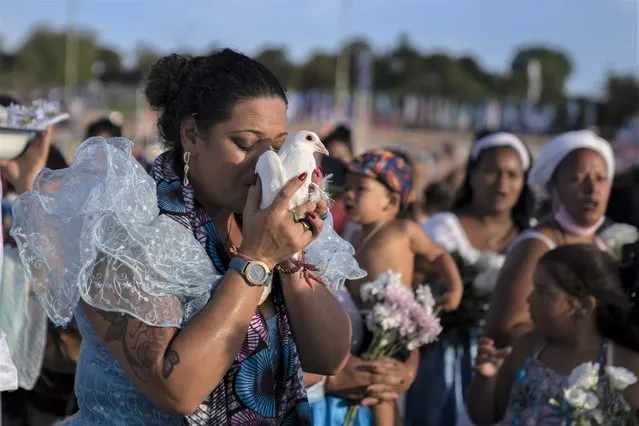 A woman kisses a pigeon as she participates in a ritual for the African sea goddess Yemanja at Ramirez Beach in Montevideo, Uruguay, Wednesday, February 2, 2022. Worshippers attend the beach on Yemanja's feast day, bearing candles, flowers, honey and fruit to honor the sea goddess. (Photo by Matilde Campodonico/AP Photo)