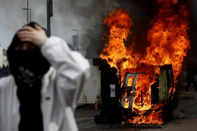 A masked protester stands in front of a burning car during clashes at a demonstration as part of the tenth day of nationwide strikes and protests against French government's pension reform in Nantes, France on March 28, 2023. (Photo by Stephane Mahe/Reuters)