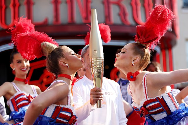 Performers kiss the Olympic Torch as Julien Segui carries the Olympic Torch at Moulin Rouge during the second day of the Paris 2024 Olympic Torch Relay on July 15, 2024 in Paris, France. (Photo by Maja Hitij/Getty Images)