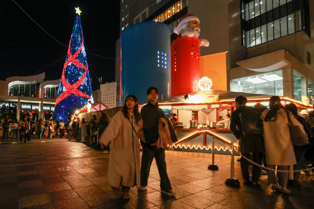 A couple walks past a Christmas tree decorated with LED lamps at Umeda Sky Building during the Christmas shopping season on December 18, 2025 in Osaka, Japan. Christmas has become a popular and busy shopping season over the past few decades. Many shops and shopping malls are decorated with seasonal greetings and offer special discounts to customers. Colorful illuminations and seasonal decorations adorn various areas of Osaka, creating a festive atmosphere. (Photo by Buddhika Weerasinghe/Getty Images)