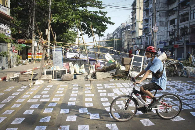 A man rides past a blocked road in Yangon, Myanmar, Tuesday, March 2, 2021. Police in Myanmar’s biggest city fired tear gas Monday at defiant crowds who returned to the streets to protest last month's coup, despite reports that security forces had killed at least 18 people a day earlier. (Photo by AP Photo/Stringer)
