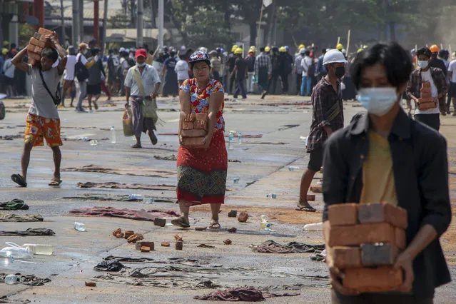 People carry bricks to help anti-coup protesters to build makeshift barricades in Yangon, Myanmar Thursday, March 11, 2021. (Photo by AP Photo/Stringer)