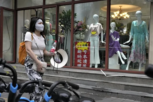 A woman walks past a store with a sign which reads “Clearing at a lost, left-over sizes clearance” at a store in Beijing, Thursday, July 27, 2023. Chinese leader Xi Jinping's government is promising to drag the economy out of a crisis of confidence aggravated by tensions with Washington, wilting exports, job losses and anxiety among foreign companies about an expanded anti-spying law. (Photo by Ng Han Guan/AP Photo)