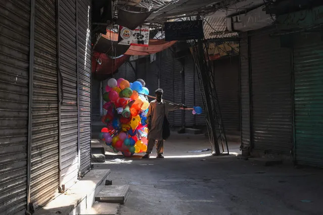 A balloon vendor walks past a shuttered market in Lahore on April 11, 2021, as a lockdown was imposed to control the spread of the Covid-19 coronavirus. (Photo by Arif Ali/AFP Photo)