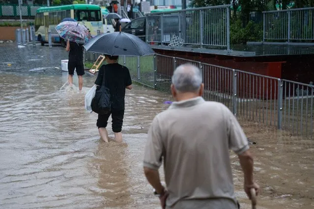 People walk on a flooded road in Hong Kong on September 8, 2023. (Photo by Bertha Wang/AFP Photo)