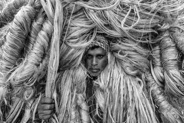 “The Man of Golden Fibers”. Workers appear to be wearing large golden wigs as they carry 50kg bundles of jute on their shoulders. Their bodies are enveloped, with only their faces visible. (Photo by Azim Khan Ronnie/International Portrait Photographer of the Year)