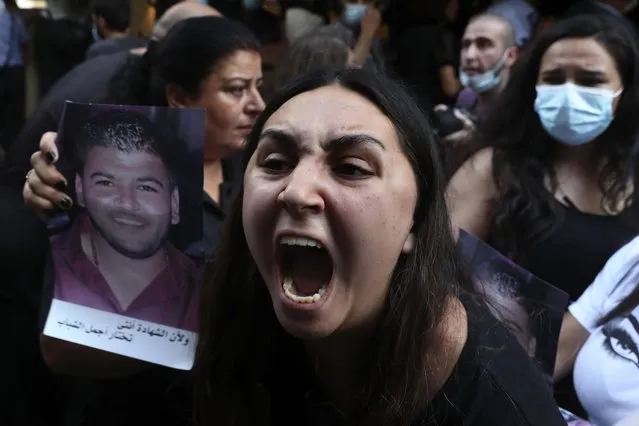 A woman whose brother was killed during last year's massive blast at Beirut's seaport, holds a portrait of him as she chants slogans during a protest outside the home of caretaker Interior Minister Mohamed Fehmi, in Beirut, Lebanon, Tuesday, July 13, 2021. (Photo by Bilal Hussein/AP Photo)