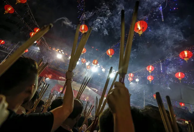 Devotees, pictured under a rows of lanterns, hold up joss sticks while waiting outside the Kwang Im Tho temple in Singapore, 07 February 2016. The country's majority Chinese population will celebrate the Lunar New Year on 08 February, ushering in the year of the Fire Monkey, according to the Chinese Zodiac calendar. (Photo by Wallace Woon/EPA)