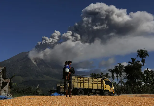 A man holds his son while walking on dried corn with Mount Sinabung spewing ash in the background at Sibintun village in Karo district, November 25, 2013. (Photo by Reuters/Beawiharta)