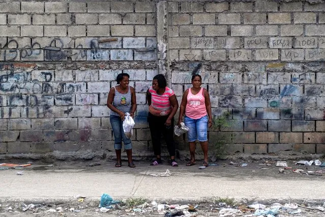 Three women stand on a sidewalk in Port-au-Prince, Haiti on July 15, 2021. (Photo by Ricardo Arduengo/Reuters)