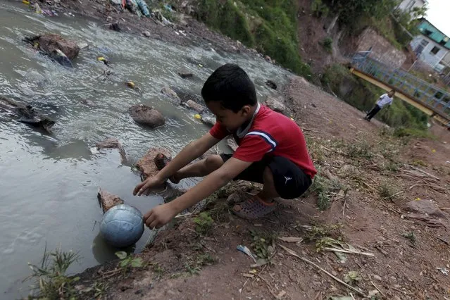 A boy grabs a ball that fell into a creek while playing football with a friend at a slum in Tegucigalpa, Honduras on January 27, 2016. (Photo by Jorge Cabrera/Reuters)