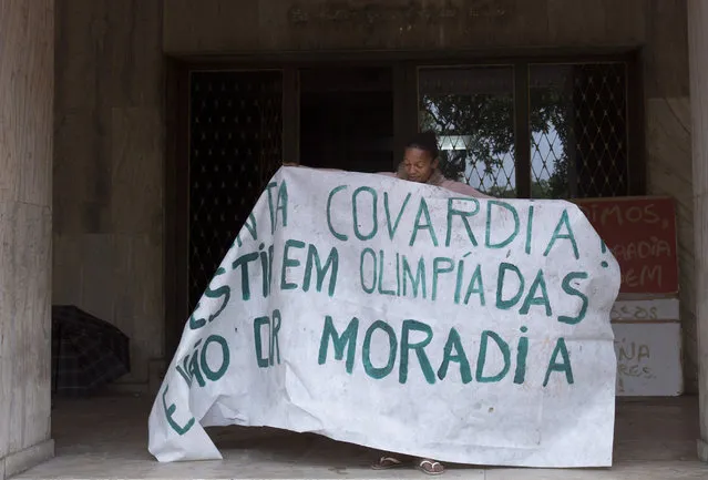 A woman holds open a banner that reads in Portuguese “Such cowardice. Investment in Olympics and not housing” to show it to the press and neighbors from inside an abandoned building in the middle class Flamengo neighborhood of Rio de Janeiro, Brazil, Tuesday, April 7, 2015. (Photo by Silvia Izquierdo/AP Photo)