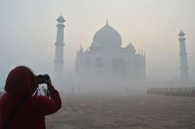 A tourist takes a picture of the Taj Mahal amid heavy smog conditions in Agra on November 23, 2023. (Photo by Pawan Sharma/AFP Photo)