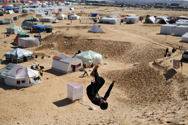 A boy does a backflip, as displaced Palestinians, who fled their houses due to Israeli strikes, take shelter in a tent camp, amid the ongoing conflict between Israel and the Palestinian Islamist group Hamas, at the border with Egypt, in Rafah in the southern Gaza Strip on February 8, 2024. (Photo by Ibraheem Abu Mustafa/Reuters)