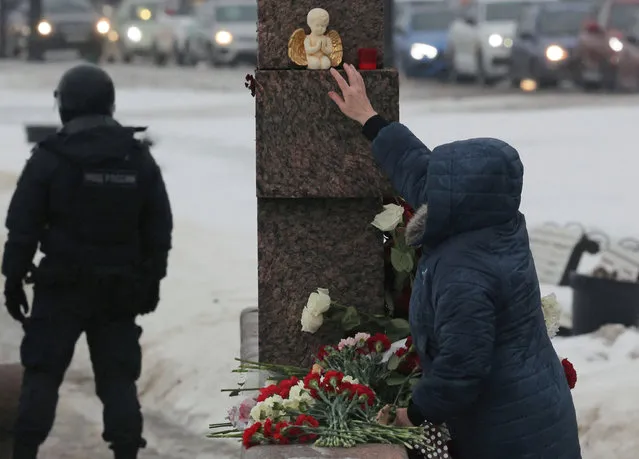 A woman reaches out to move a figure of an angel placed at the monument to the victims of political repressions in memory of Russian opposition leader Alexei Navalny, in Saint Petersburg, Russia on February 17, 2024. (Photo by Reuters/Stringer)