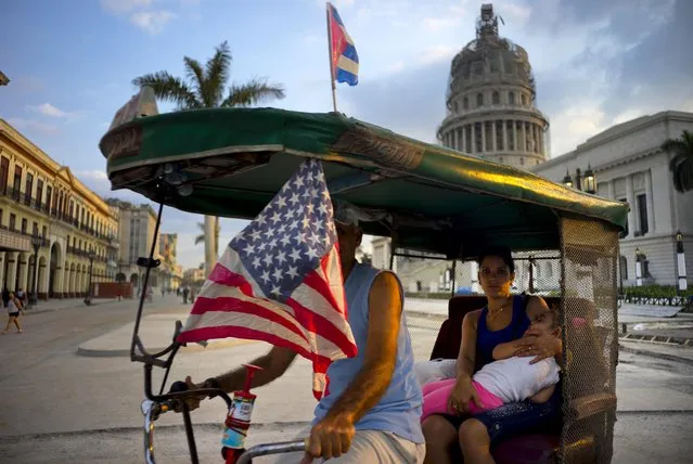 A taxi pedals his bicycle, decorated with Cuban and U.S. flags, as he transports a woman holding a sleeping girl, near the Capitolio in Havana, Cuba, Tuesday, March 15, 2016. (Photo by Ramon Espinosa/AP Photo)