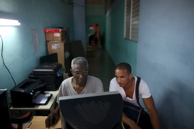Silvio Lang, 61 (L), attends to a client at an improvised office in his house where he sells prints and DVDs in Havana, March 18, 2016. (Photo by Alexandre Meneghini/Reuters)