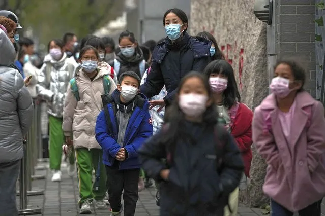 Students wearing face masks to protect from COVID-19 are escorted by a teacher as they leave school after classes in Beijing, Monday, November 29, 2021. Despite the global worry, scientists caution that it's still unclear whether the omicron COVID-19 variant is more dangerous than other versions of the virus that has killed more than 5 million people. Some countries are continuing with previous plans to loosen restrictions, with signs of reopening in Malaysia, Singapore and New Zealand. (Photo by Andy Wong/AP Photo)