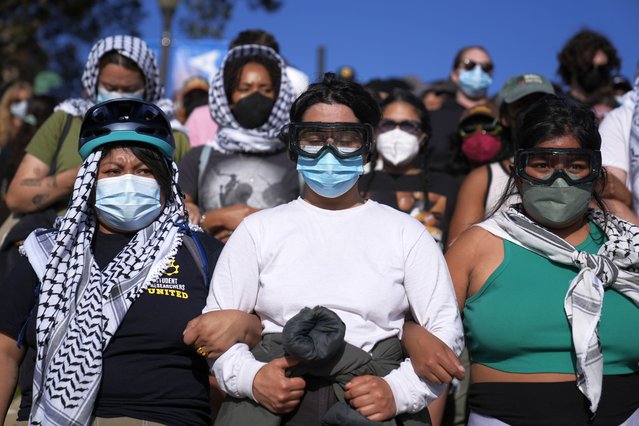 Pro-Palestinian demonstrators wearing hatta scarves and goggles lock arms forming a human chain on the UCLA campus, in Los Angeles, May 1, 2024. (Photo by Jae C. Hong/AP Photo)