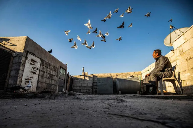 Abdulhamid Hana, a 50-year-old Syrian pigeon keeper, watches his birds on the roof of his home in Syria's eastern city of Raqa on March 13, 2021. Handed down through the generations, the practice of domesticating pigeons stretches across borders from the banks of the Nile across north Africa and beyond, with people not only training birds for competitions, but also serving them up as a dining delicacy. (Photo by Delil Souleiman/AFP Photo)