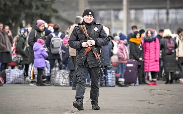A Ukrainian policeman walks on a platform backdropped by people waiting for a Kiev bound train in Kostiantynivka, the Donetsk region, eastern Ukraine, Thursday, February 24, 2022. (Photo by Vadim Ghirda/AP Photo)