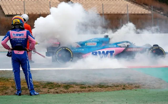 Alpine driver Fernando Alonso of Spain watches smoke pour from his car during a Formula One pre-season testing session at the Catalunya racetrack in Montmelo, just outside of Barcelona, Spain, Friday, February 25, 2022. (Photo by Joan Monfort/AP Photo)