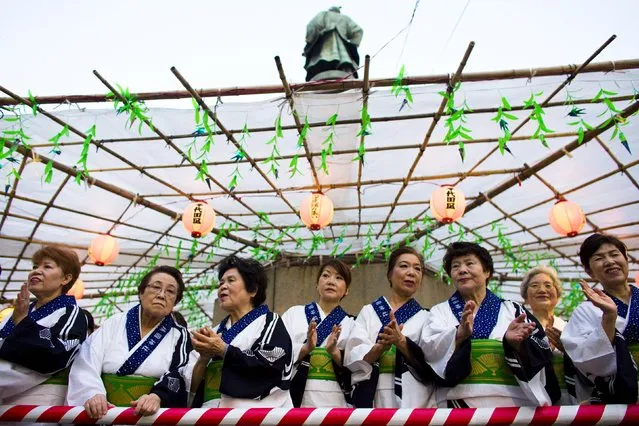 Women wearing traditional clothes watch as people carry a portable shrine during the annual Mitama Festival at the Yasukuni Shrine in Tokyo, Japan, July 13, 2015. (Photo by Thomas Peter/Reuters)