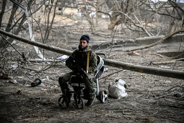 An Ukrainian serviceman sits on a baby trolley under a destroyed bridge in the city of Irpin, northwest of Kyiv, on March 13, 2022. Russian forces advance ever closer to the capital from the north, west and northeast. Russian strikes also destroy an airport in the town of Vasylkiv, south of Kyiv. A US journalist was shot dead and another wounded in Irpin, a frontline northwest suburb of Kyiv, medics and witnesses told AFP. (Photo by Aris Messinis/AFP Photo)