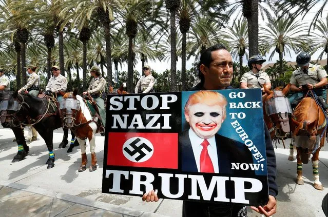 An anti-Trump demonstrator protests as Orange County Sheriff officers stand watch outdoors before Republican U.S. Presidential candidate Donald Trump speaks at a campaign event in Anaheim, California U.S. May 25, 2016. (Photo by Mike Blake/Reuters)