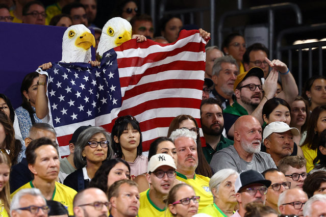 United States fans wearing eagle masks and holding the flag cheer on as the United States plays Brazil in the women's volleyball semifinals on August 8, 2024. (Photo by Siphiwe Sibeko/Reuters)