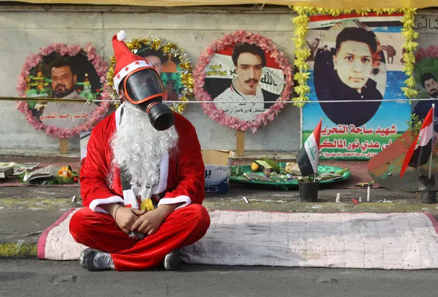 An Iraqi demonstrator wearing a Santa Claus costume and a gas mask sits on a blanket in the capital Baghdad's Tahrir Square, amid ongoing anti-government protests, on December 6, 2019. Behind him are portraits of killed demonstrators. Tahrir has become a melting pot of Iraqi society, occupied day and night by thousands of demonstrators angry with the political system in place since the aftermath of the US-led invasion of 2003 and Iran's role in propping it up. (Photo by Ahmad Al-Rubaye/AFP Photo)