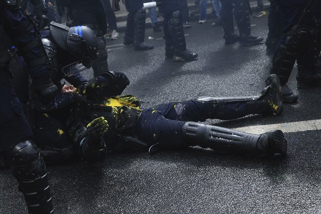 A riot police officer is lying on the pavement during a demonstration in Paris, Monday, May 1, 2023. Across France, thousands marched in what unions hope are the country's biggest May Day demonstrations in years, mobilized against President Emmanuel Macron's recent move to raise the retirement age from 62 to 64. (Photo by Aurelien Morissard/AP Photo)