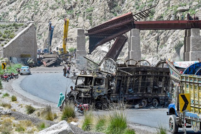 Residents stand beside a charred vehicle near a collapsed railway bridge the morning after a blast by separatist militants at Kolpur in Bolan district, Balochistan province on August 27, 2024. Pakistani forces hunted separatist militants on August 27, who killed dozens when they pulled passengers off buses, blew up a bridge and stormed a hotel a day earlier. Militants in Balochistan took control of a highway and shot dead 23 people, mostly labourers from neighbouring Punjab province, attacked the hotel and the railway bridge which connects Balochistan to the rest of Pakistan. (Photo by Banaras Khan/AFP Photo)