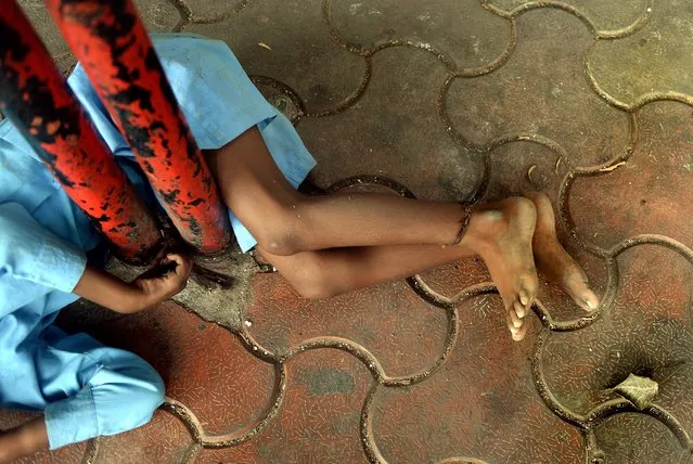 In this photograph taken on May 20, 2014 nine year old Indian boy Lakhan Kale is tied with a cloth rope around his ankle, to a bus-stop pole in Mumbai. (Photo by Punit Paranjpe/AFP Photo)