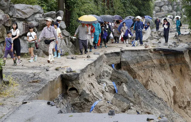 In this July 6, 2017 photo,  local residents walk on a damaged road to a safer place following the flooding caused by heavy rain in Asakura, Fukuoka prefecture, southwestern Japan. Troops worked Thursday to rescue hundreds of people stranded by flooding in southern Japan. (Photo by Takuto Kaneko/Kyodo News via AP Photo)
