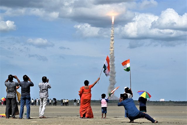 People wave Indian flags as an Indian Space Research Organisation (ISRO) rocket carrying the Chandrayaan-3 spacecraft lifts off from the Satish Dhawan Space Centre in Sriharikota, an island off the coast of southern Andhra Pradesh state on July 14, 2023. India on July 14 launched a rocket seeking to land an unmanned spacecraft on the surface of the Moon, a live feed showed, its second attempt to become only the fourth country to do so. (Photo by R. Satish Babu/AFP Photo)