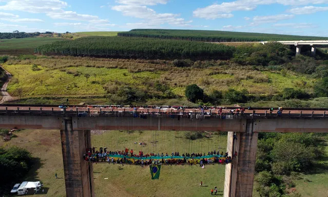 A group of 90 people eat at a barbecue as they sit on a table while suspended under a bridge using rapelling techniques in Limeira, Brazil, July 30, 2017. (Photo by Paulo Whitaker/Reuters)