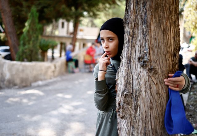 Displaced girl looks on behind a tree outside a school turned into shelter, amid ongoing hostilities between Hezbollah and Israeli forces in Baabda, Lebanon on October 31, 2024. (Photo by Yara Nardi/Reuters)