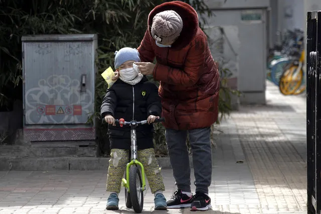 A woman wipes the face of a child on the streets of Beijing on Thursday, March 12, 2020. For most people, the new coronavirus causes only mild or moderate symptoms. For some it can cause more severe illness, especially in older adults and people with existing health problems. (Photo by Ng Han Guan/AP Photo)