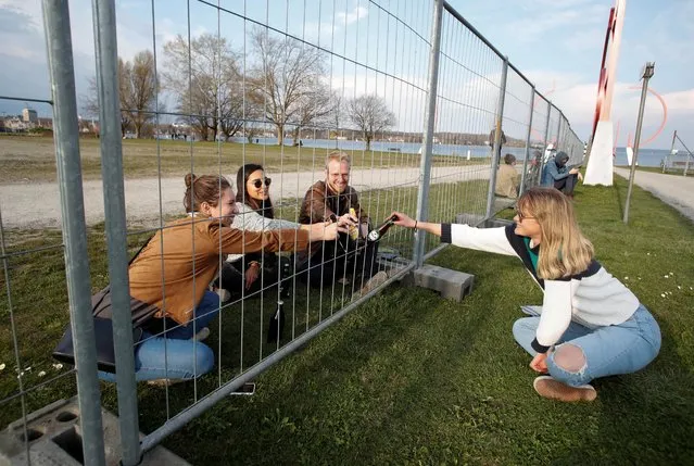 Friends clink with beer bottles through a fence built by German authorities on the German-Swiss border in a park on the banks of Lake Constance in Kreuzlingen, Switzerland on March 20, 2020. (Photo by Arnd Wiegmann/Reuters)