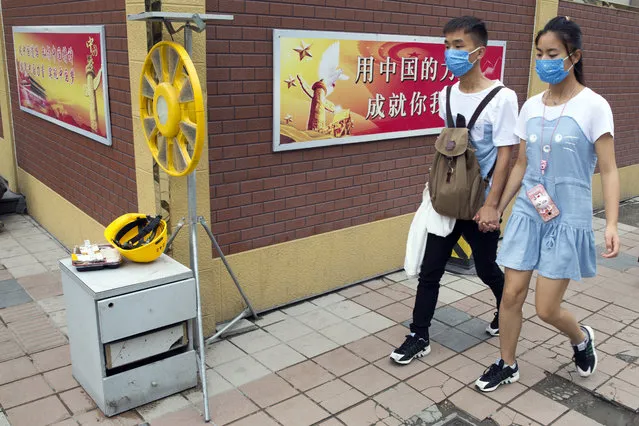 In this Friday, July 15, 2016 photo, a Chinese couple wearing masks to protect against air pollution walk past a Chinese government propaganda slogan for the “Chinese Dream” in Beijing. Beijing's notoriously awful air quality improved significantly in the first half of the year, with actions taken to curb the city's heavy pollution having a positive effect, officials in the Chinese capital said Monday, July 19, 2016. (Photo by Ng Han Guan/AP Photo)